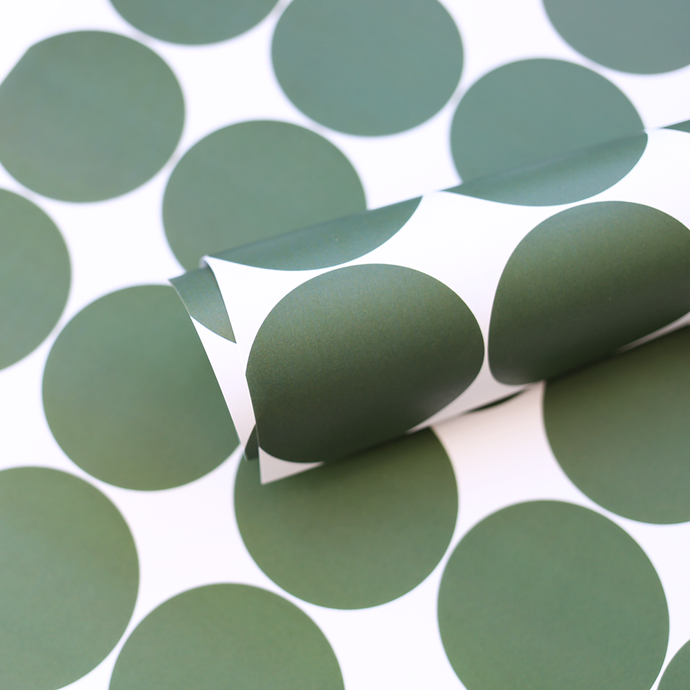 A close-up of a rolled sheet of wrapping paper or fabric featuring a bold pattern of large sage green circles on a white background.